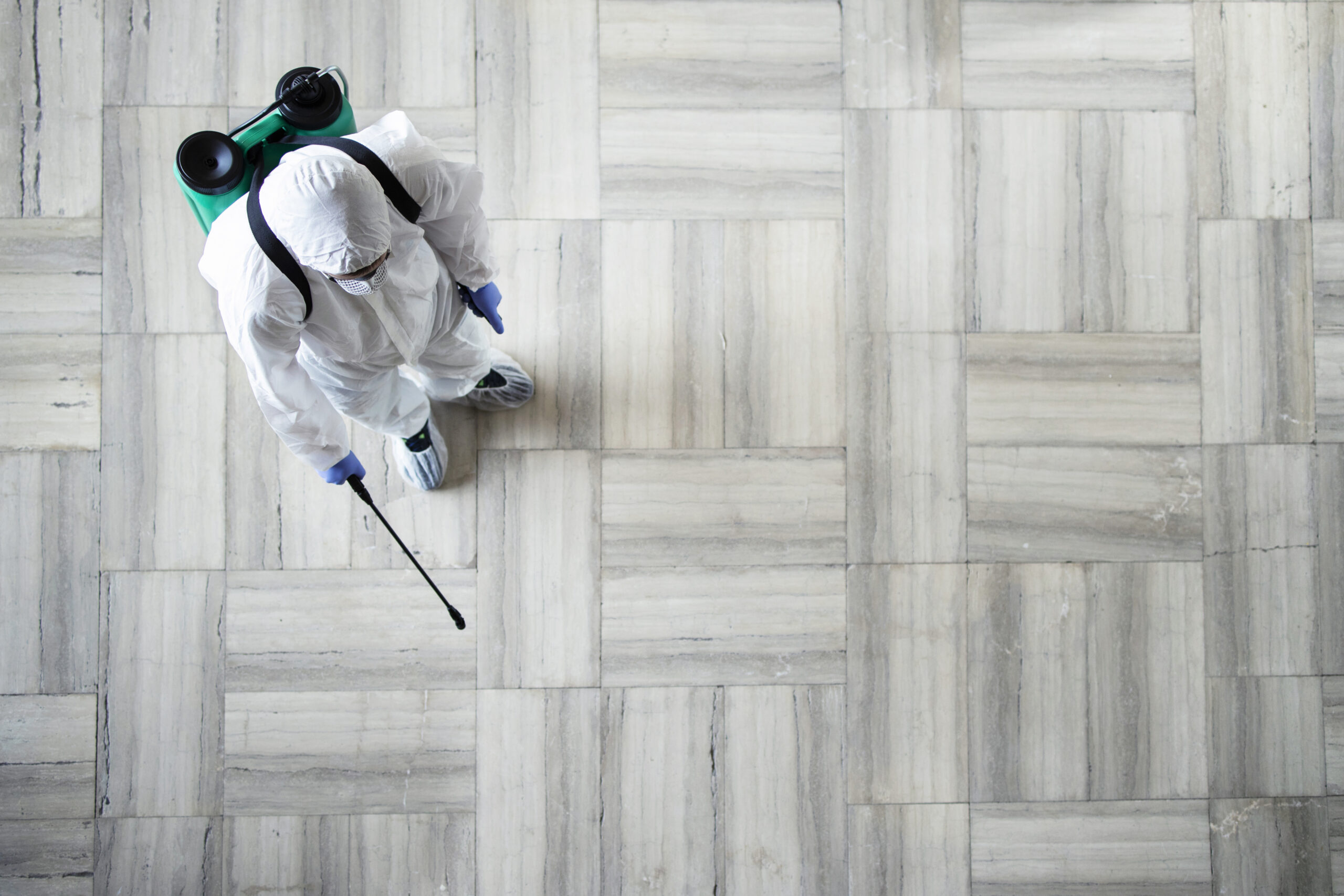 Unrecognizable person in white chemical protection suit doing disinfection of public areas to stop spraying highly contagious corona virus.