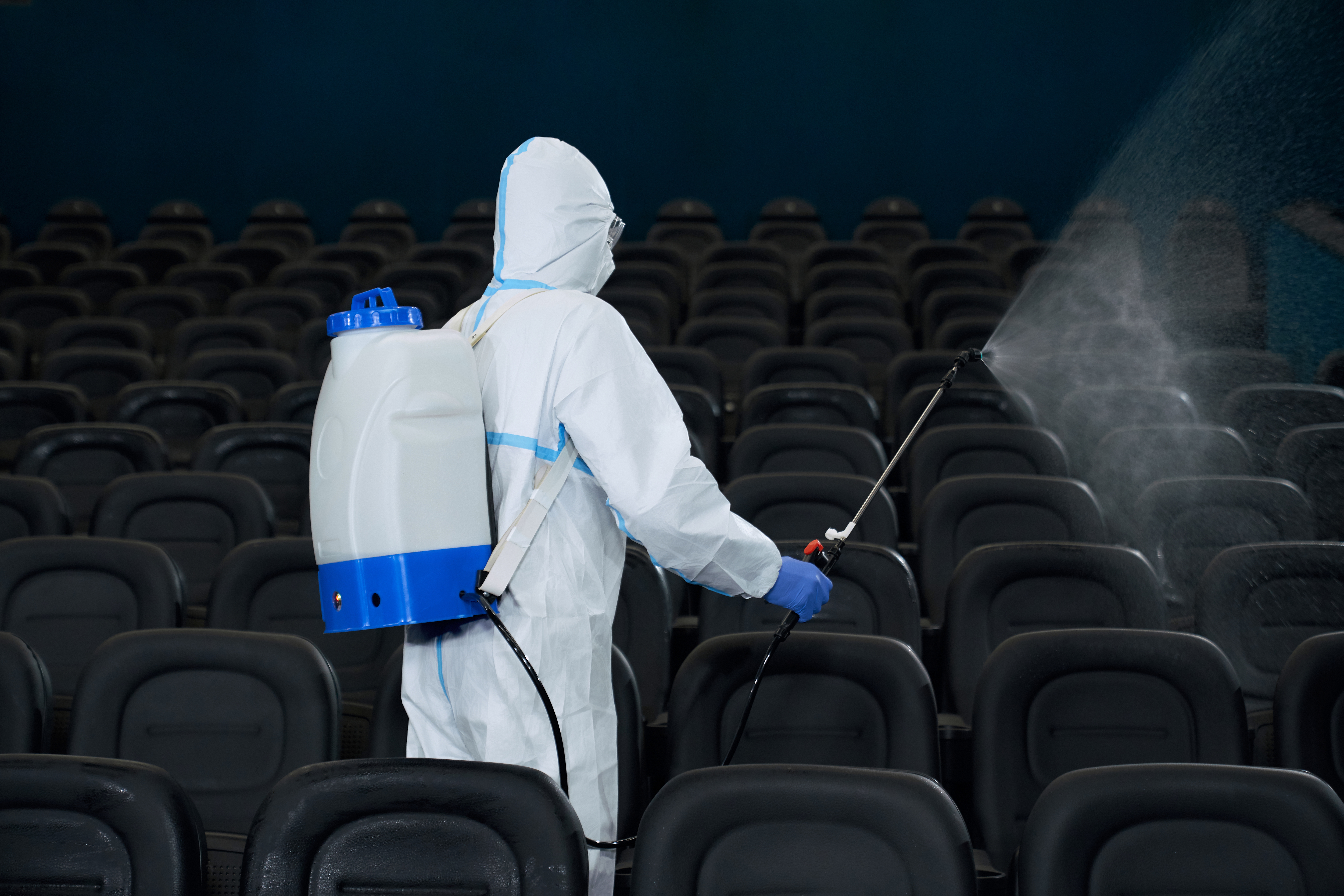 Worker in protective clothes against coronavirus with special equipment for disinfection cleaning cinema hall. Concept of protective against virus.